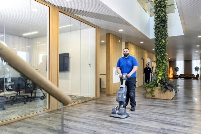 Schoonmaker reinigt een kantoorgang met een vloermachine
